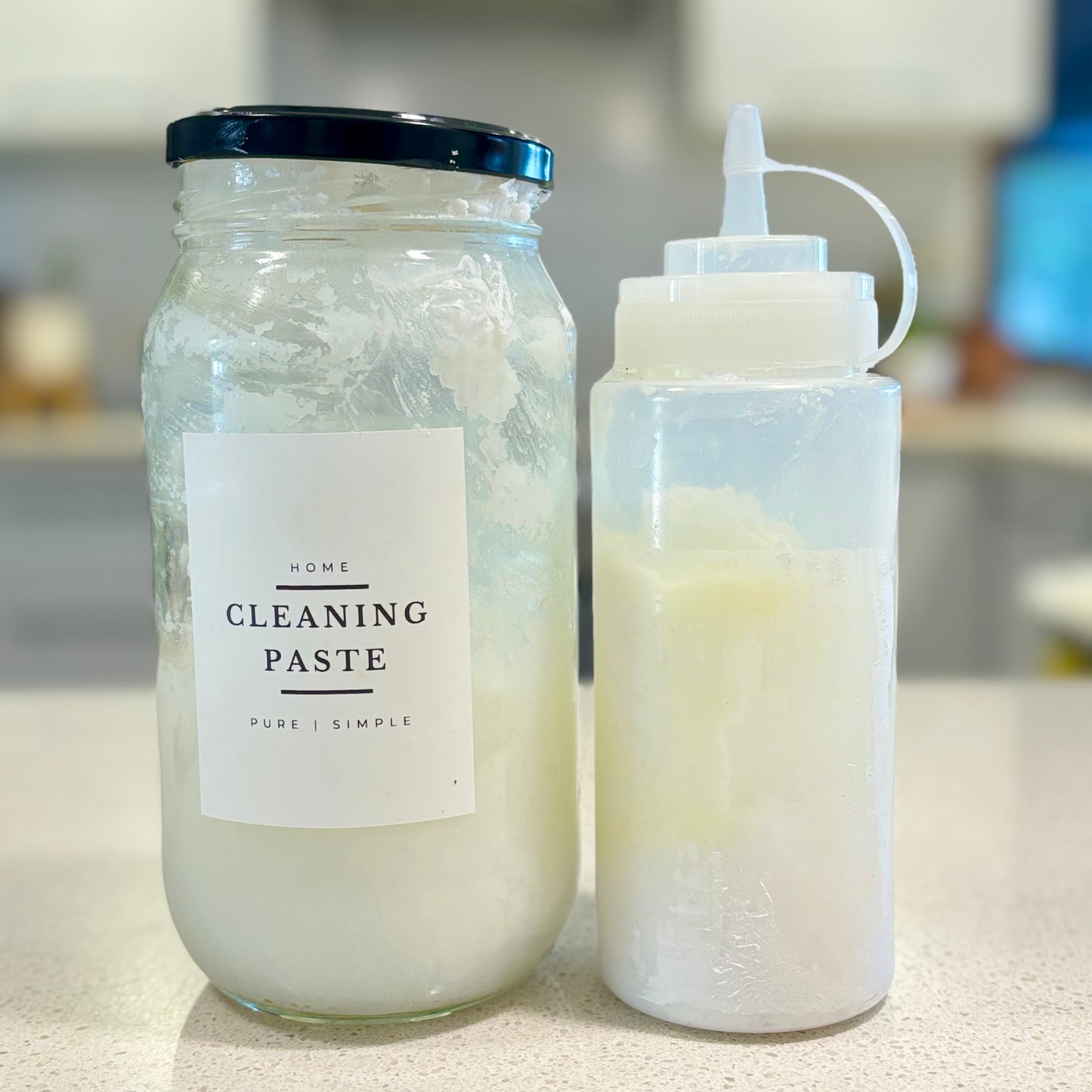 Glass jar labeled 'Home Cleaning Paste' next to a squeeze bottle on a countertop.