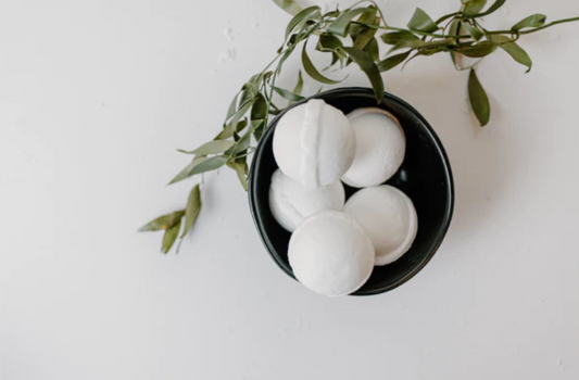 A plain grey background and a black bowl with white handmade fizzy bath bombs with a  eucalyptus branch to show its natural. Its a very clean crisp image and used for a the cover of a blog  on  How to make fizzy Bath, Toilet & Shower Bombs