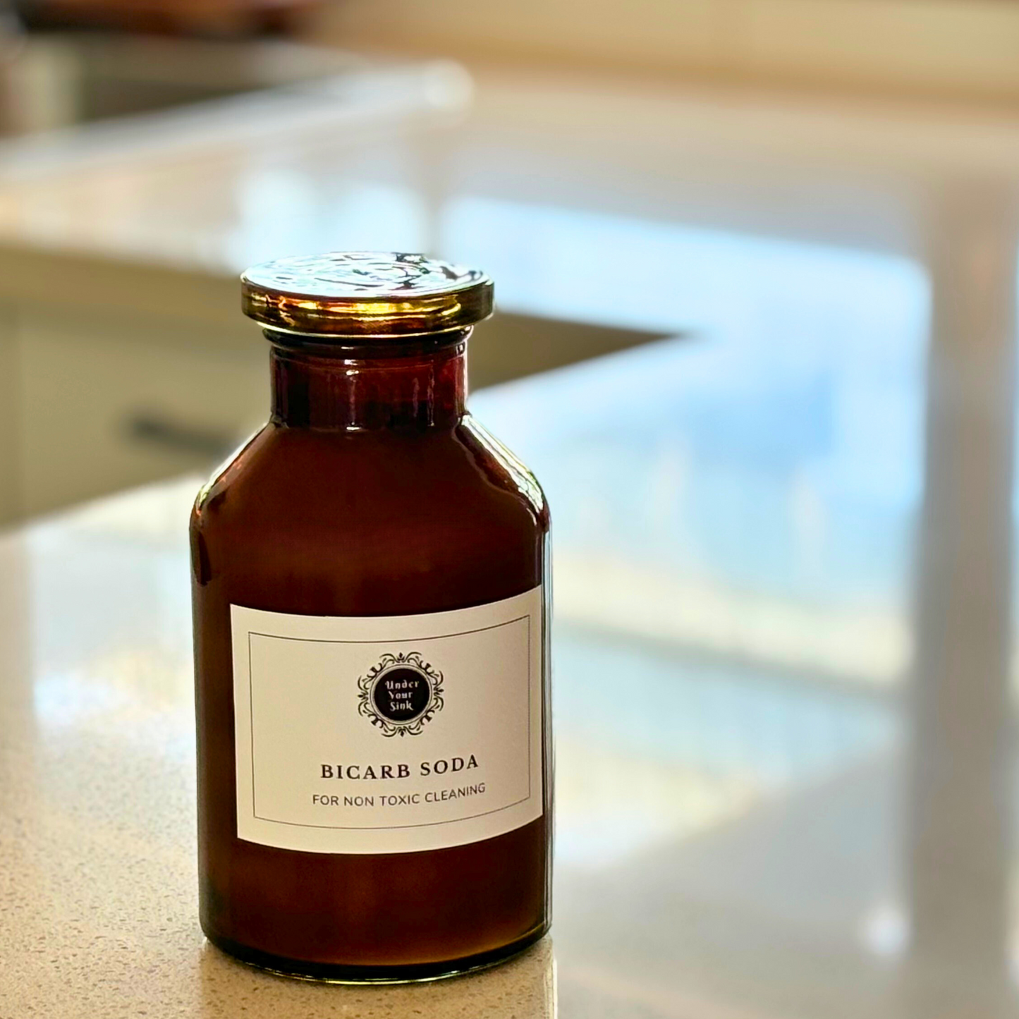 An amber glass Apothecary Jar with a vintage antique look. It has a white label with Under your Sink Logo and description Bicarb- all round Eco-cleaner – mild strength alkali, It’s filled with white crystalline Bicarb granules inside. Background is of a kitchen and it’s a clean image to show green cleaning. This is a product image for website as this is for sale in various sizes, online with Australia wide delivery.