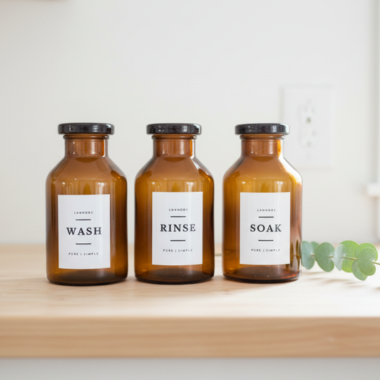 Three amber glass bottles labeled 'Wash', 'Rinse', and 'Soak' on a wooden surface with a light background.