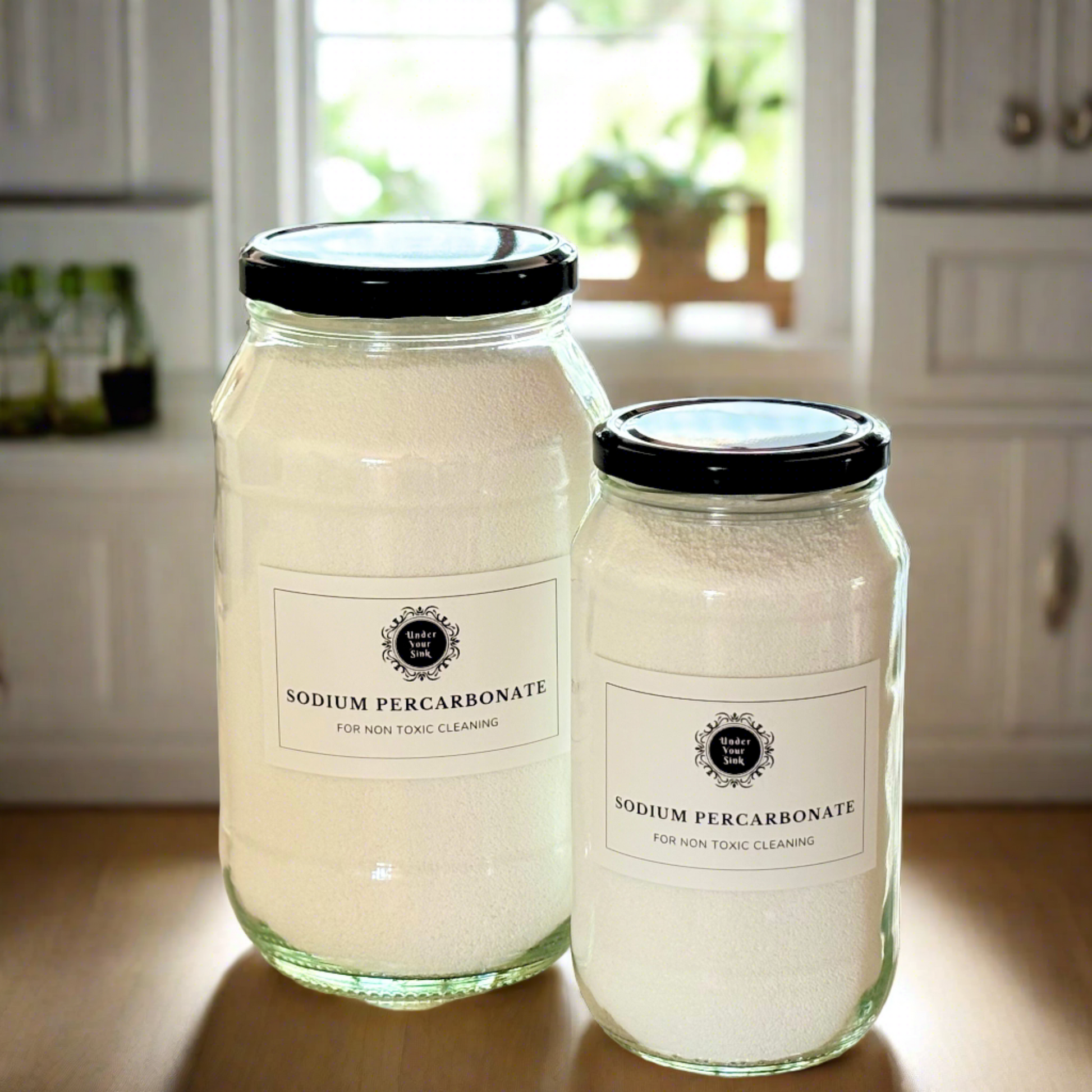 Two clear glass jars, one larger (2Litres) and one smaller (1litre). They both have simple white label with Under your Sink Logo and description Percarbonate - all round Eco-cleaner - Oxygen bleach. They are filled with white crystalline percarbonate granules inside. Background is of a kitchen and it’s a clean image to show green cleaning. This is a product image for website as this is for sale in various sizes, online with Australia wide delivery.