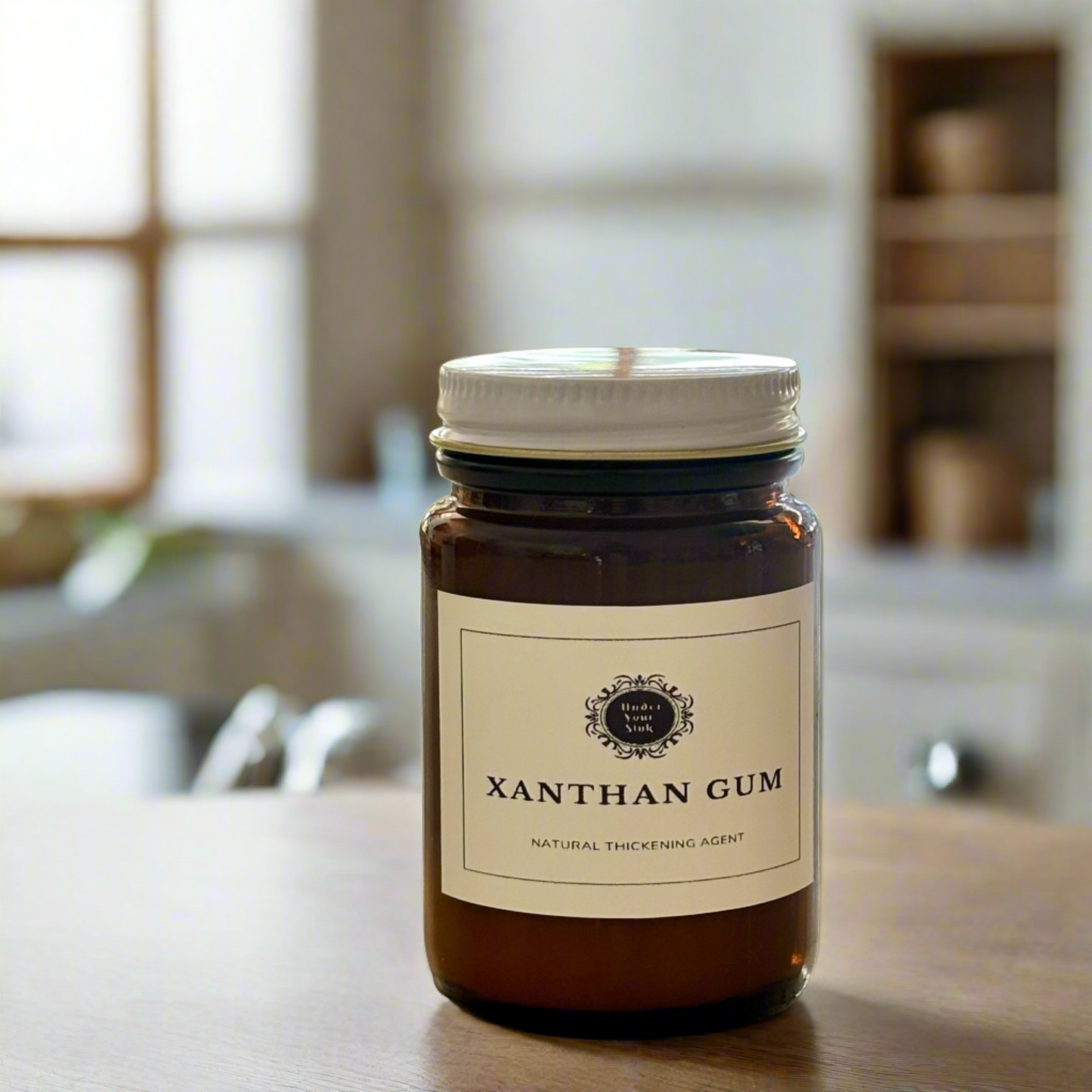 An amber glass jar with a simple white label with Under your Sink Logo and description Xanthan Gum – natural thickening agent. Set in a kitchen with blurred background and focus on the jar. It is a product image for website as this is for sale in various sizes, online with Australia wide delivery.