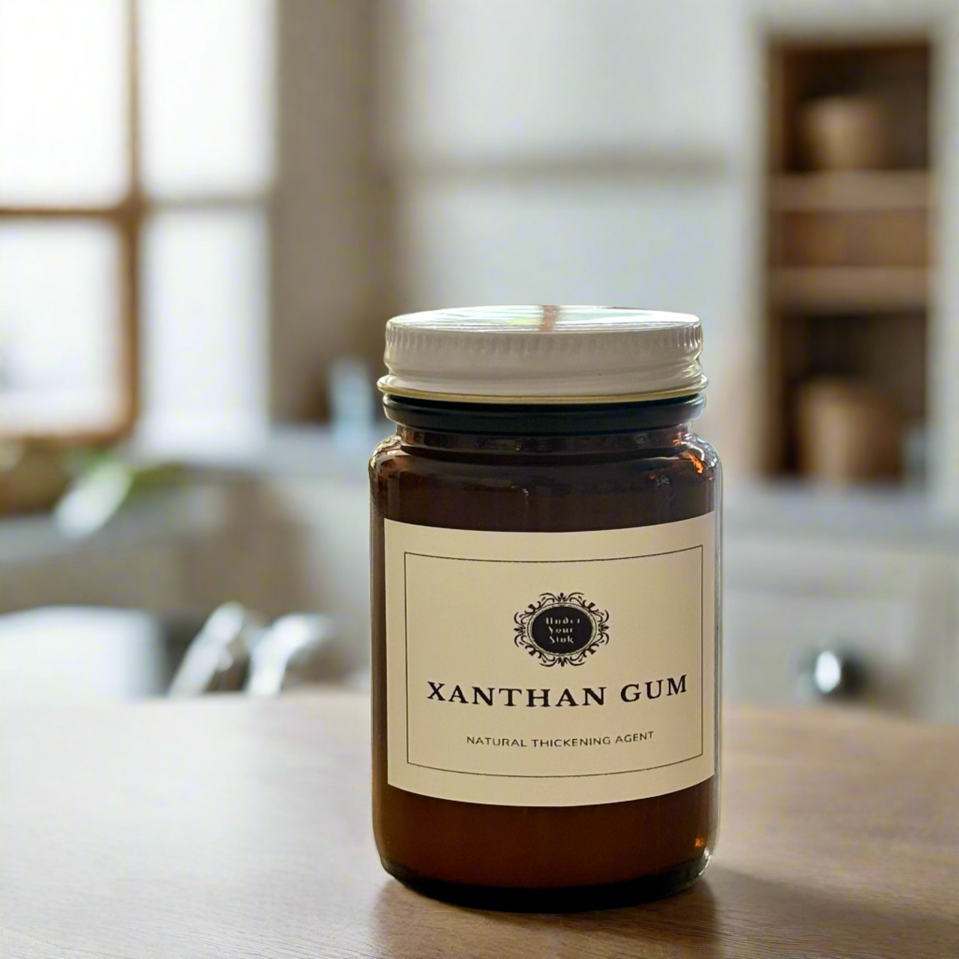 An amber glass jar with a simple white label with Under your Sink Logo and description Xanthan Gum – natural thickening agent. Set in a kitchen with blurred background and focus on the jar. It is a product image for website as this is for sale in various sizes, online with Australia wide delivery.
